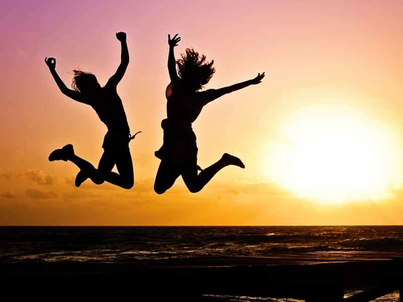 Two people jumping with sunset behind them